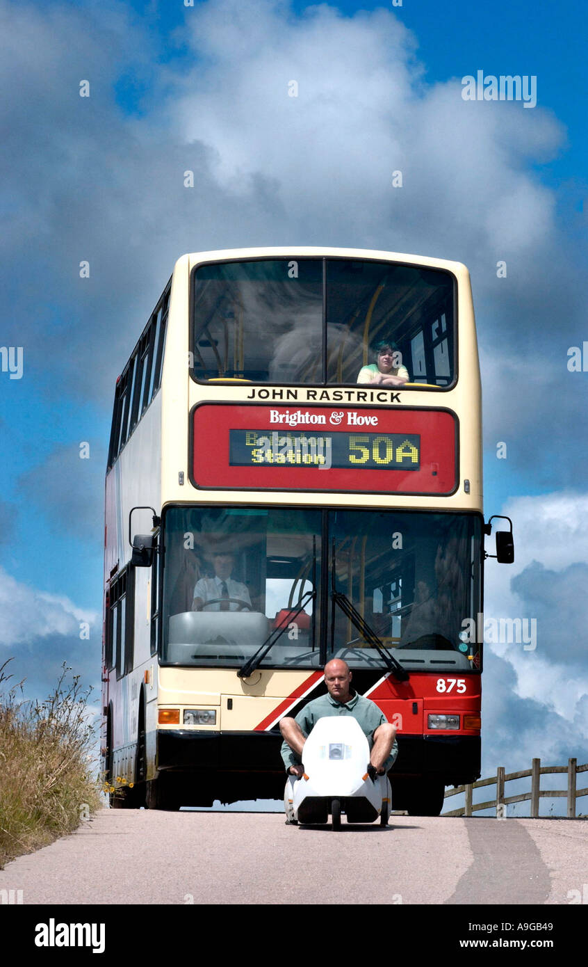 Ein Doppeldecker-Bus wartet geduldig auf einen unterlegenen Sinclair C5 auf die Braue des Hügels crest Stockfoto
