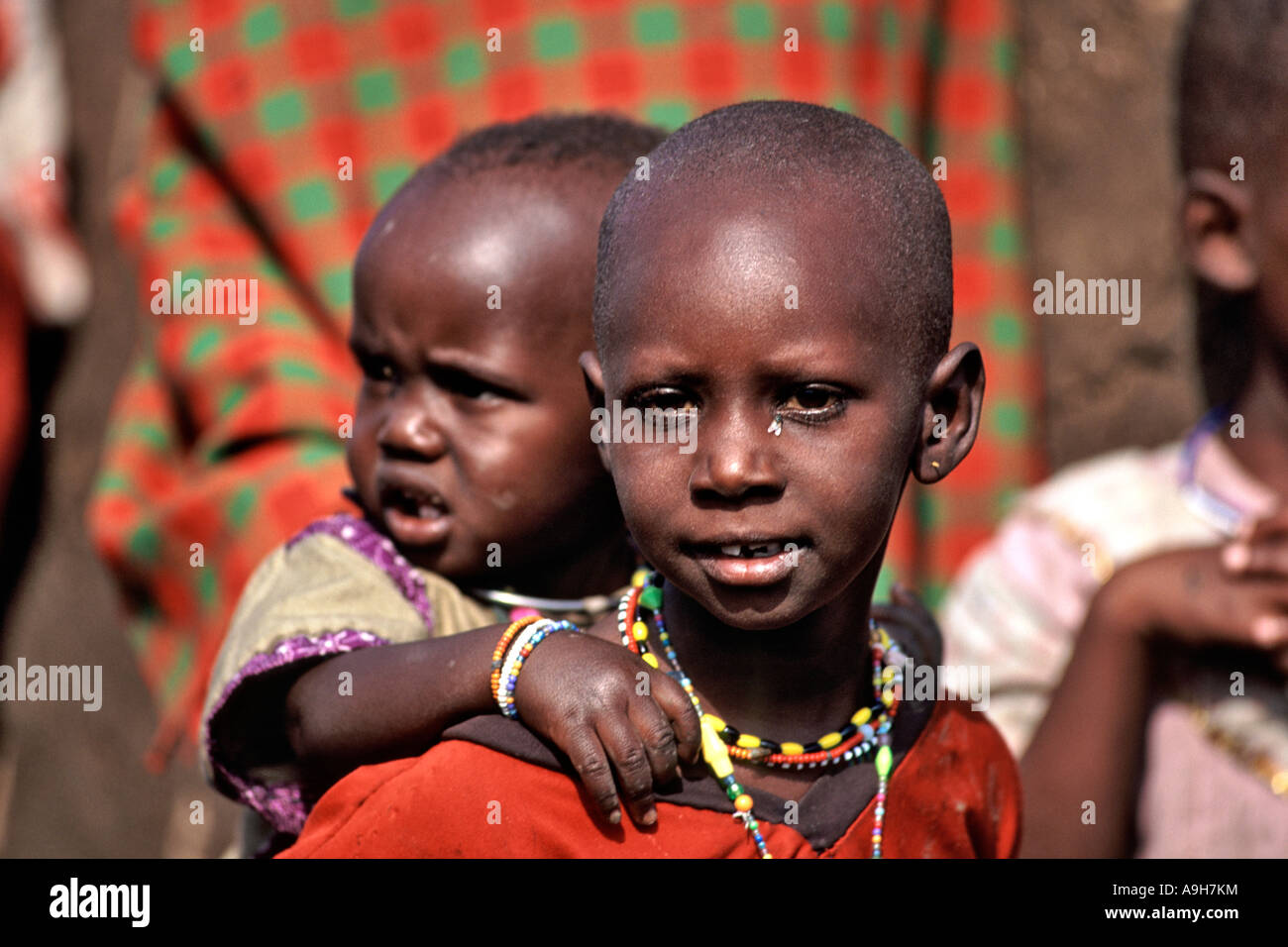 Ein Junge Masai-Mädchen trägt ein Kind auf dem Rücken in der Masai Mara-Region Kenias. Stockfoto