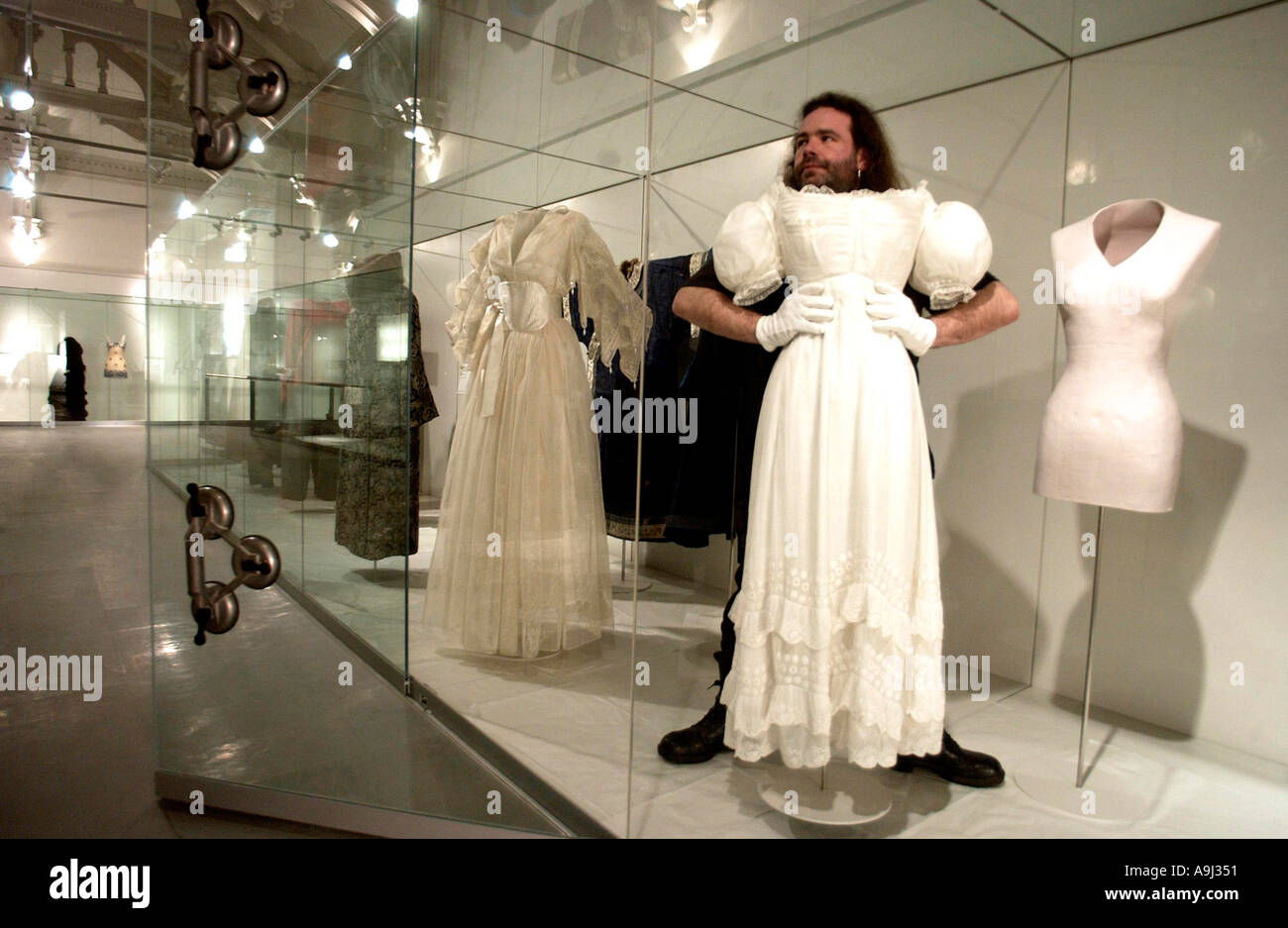 Kurator sieht aus, als ob er ein zartes Regency-Kleid trägt, als er es in der Kostümgalerie des Brighton Museums installiert Stockfoto