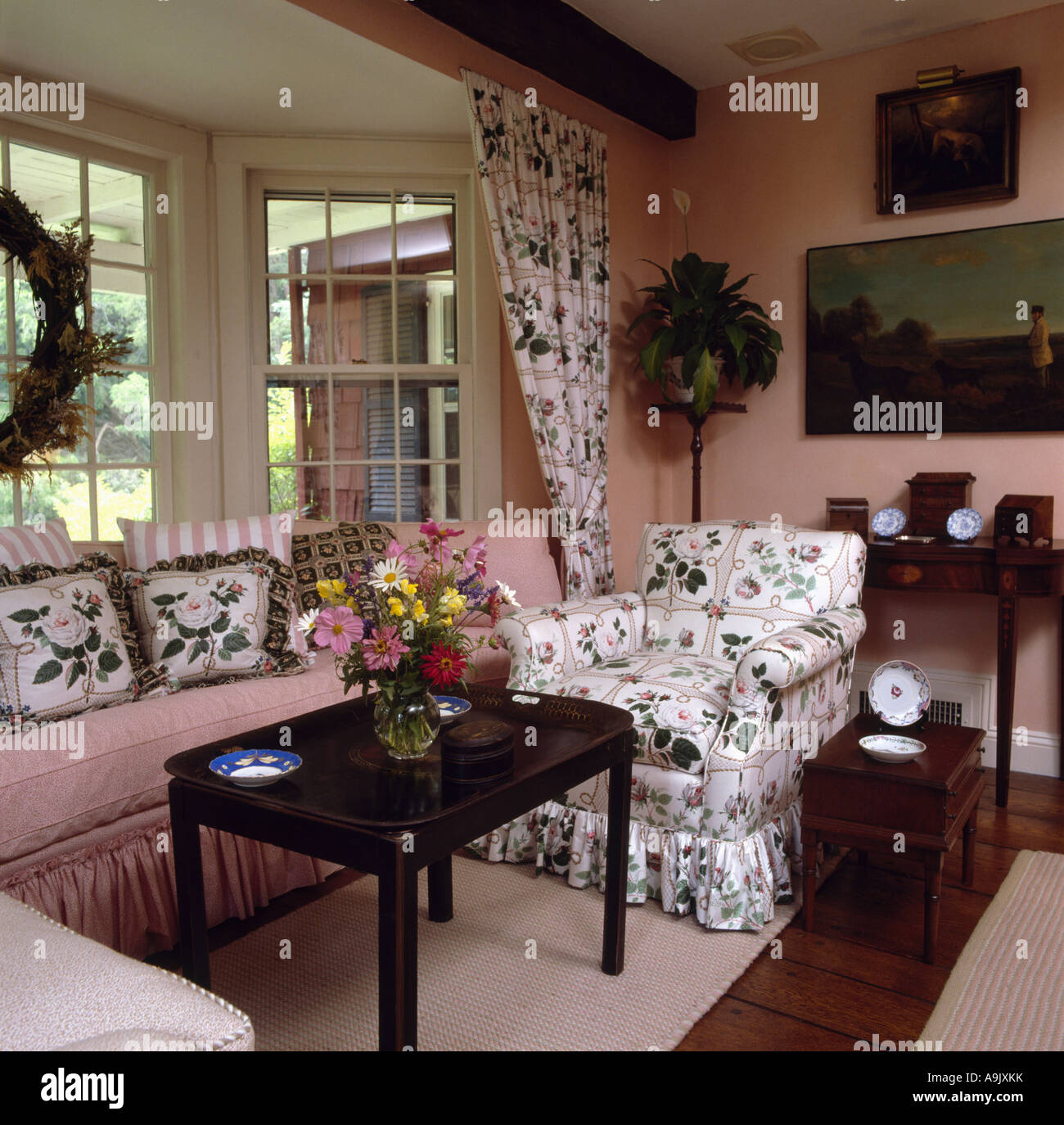 Rosa Rose-gemusterten Sessel und einem kleinen antiken Tisch durch Sitz mit floralen und rosa Kissen im Erker des Landes livingroom Stockfoto