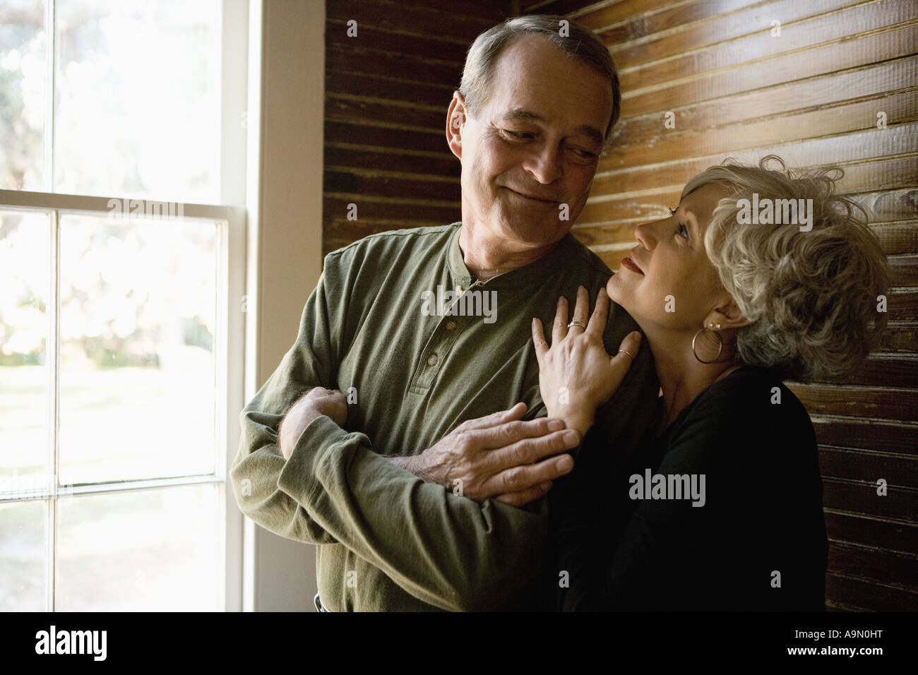 Liebevolle älteres Paar in abgedunkelten Raum neben Fensterrahmen Stockfoto