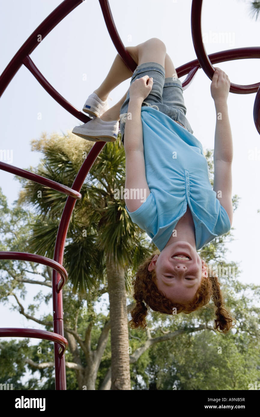 Mädchen hängt kopfüber an Klettergerüst auf einem Spielplatz Stockfoto