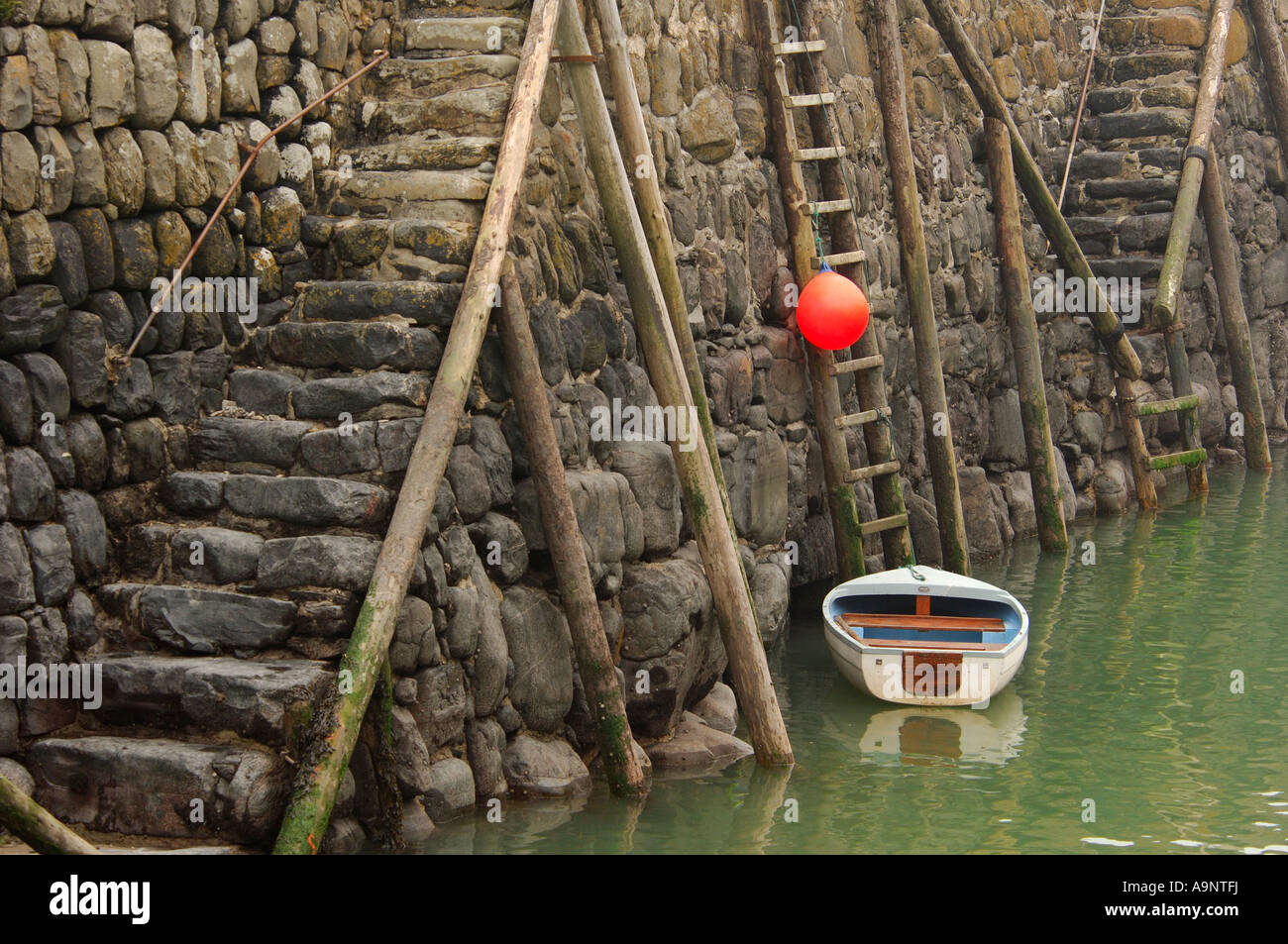 Kleine weiße Beiboot und leuchtend orange Boje an der Hafenmauer historischen 14. Jahrhundert aus Stein gebaut, in Clovelly North Devon gesichert Stockfoto