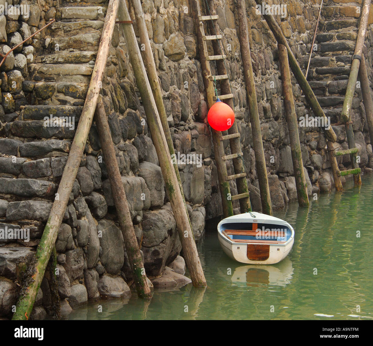 Kleine weiße Beiboot und leuchtend orange Boje an der Hafenmauer historischen 14. Jahrhundert aus Stein gebaut, in Clovelly North Devon gesichert Stockfoto