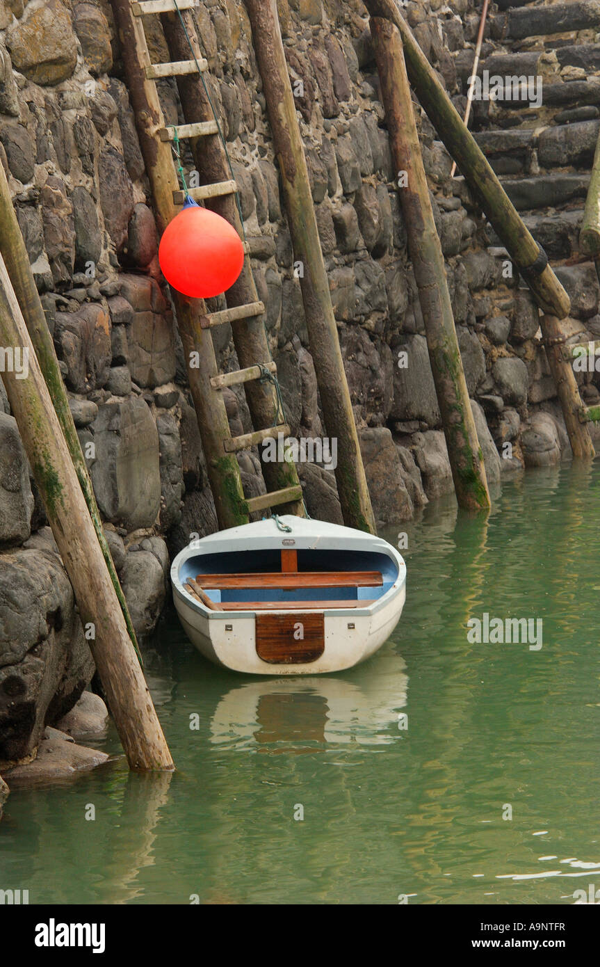 Kleine weiße Beiboot und leuchtend orange Boje an der Hafenmauer historischen 14. Jahrhundert aus Stein gebaut, in Clovelly North Devon gesichert Stockfoto