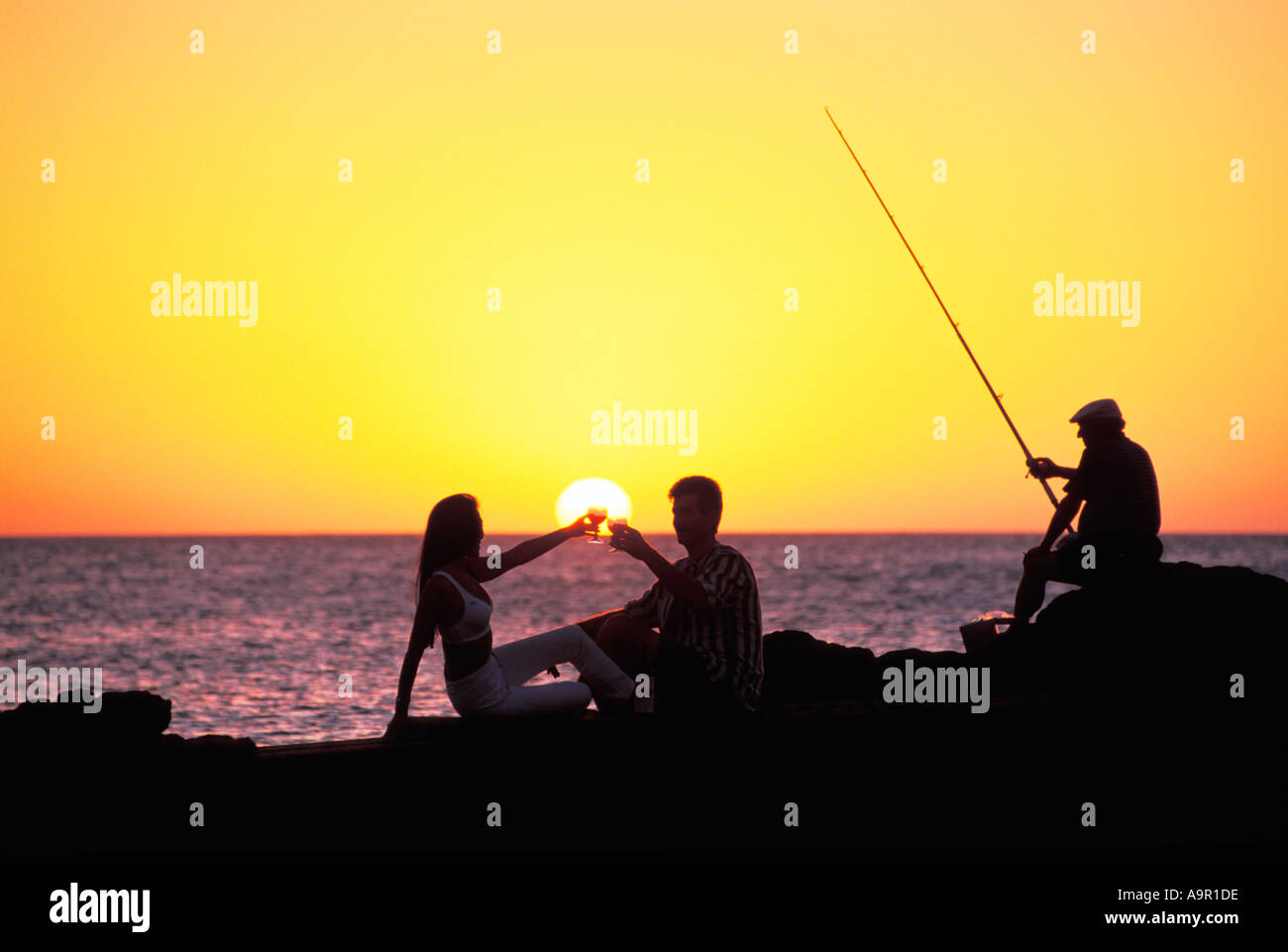 Paar am Ufer Toasten bei Sonnenuntergang mit Fischer Stockfoto