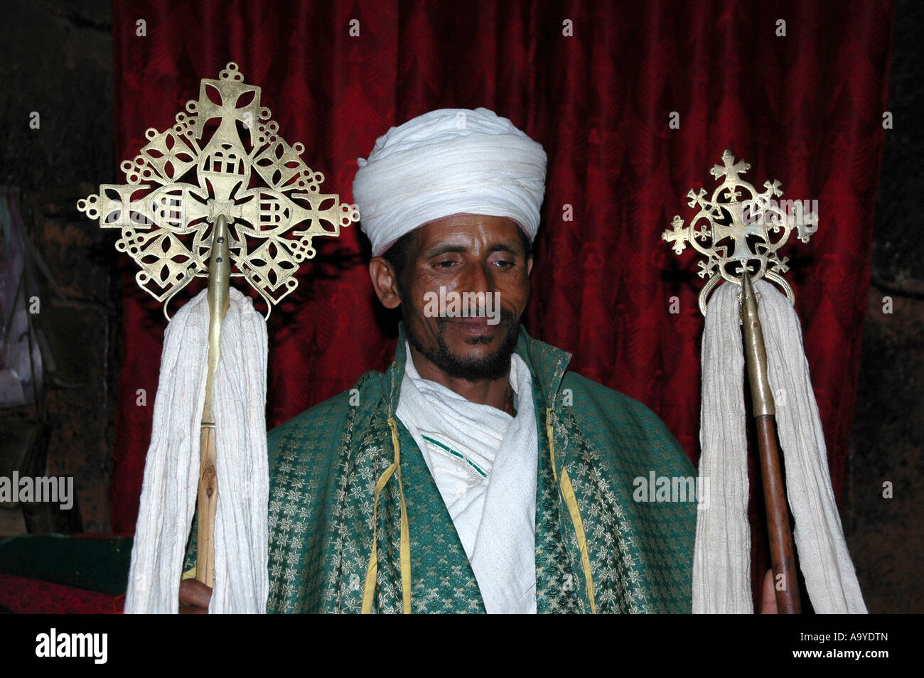 Priester, bekleidet mit einem grünen Umhang trägt zwei kunstvolle Kreuze Felsenkirche Lalibela, Äthiopien Stockfoto