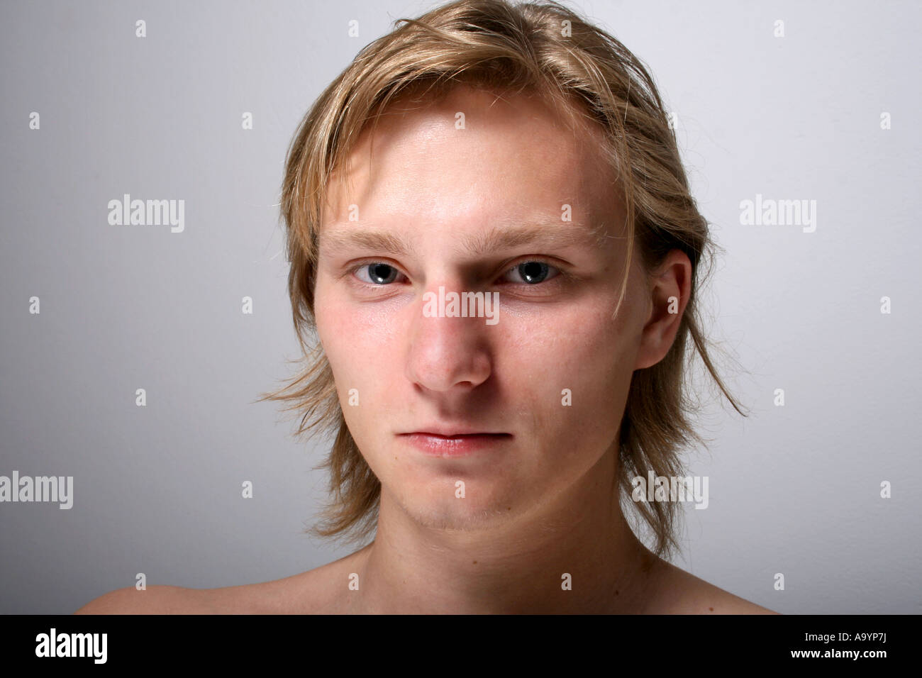 Nahporträt eines jungen Mannes mit ernstem Ausdruck vor einem schlichten Hintergrund, das natürliche Merkmale und raue Emotionen betont. Stockfoto