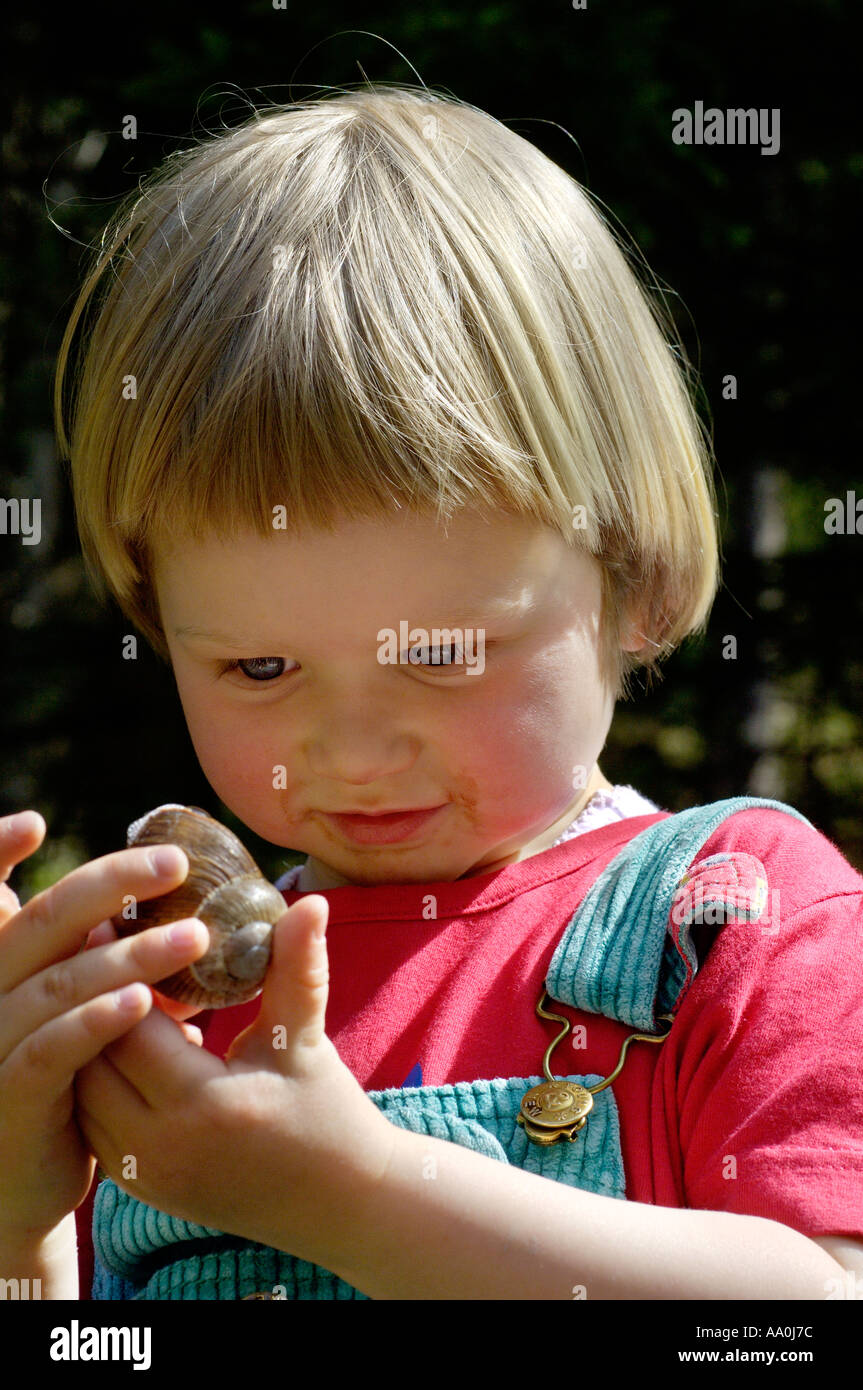 Ein drei Jahres altes Mädchen untersucht eine Schnecke Stockfoto