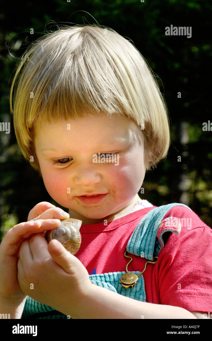 Ein drei Jahres altes Mädchen untersucht eine Schnecke Stockfoto