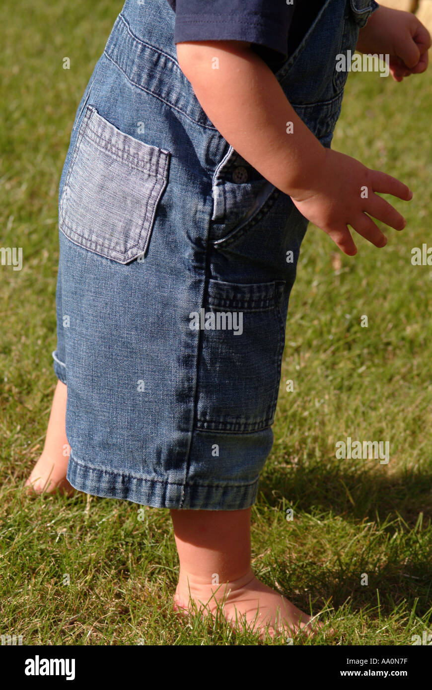 Nahaufnahme eines Kleinkindes barfuß auf dem Rasen und tragen Jeans-Latzhose  Stockfotografie - Alamy
