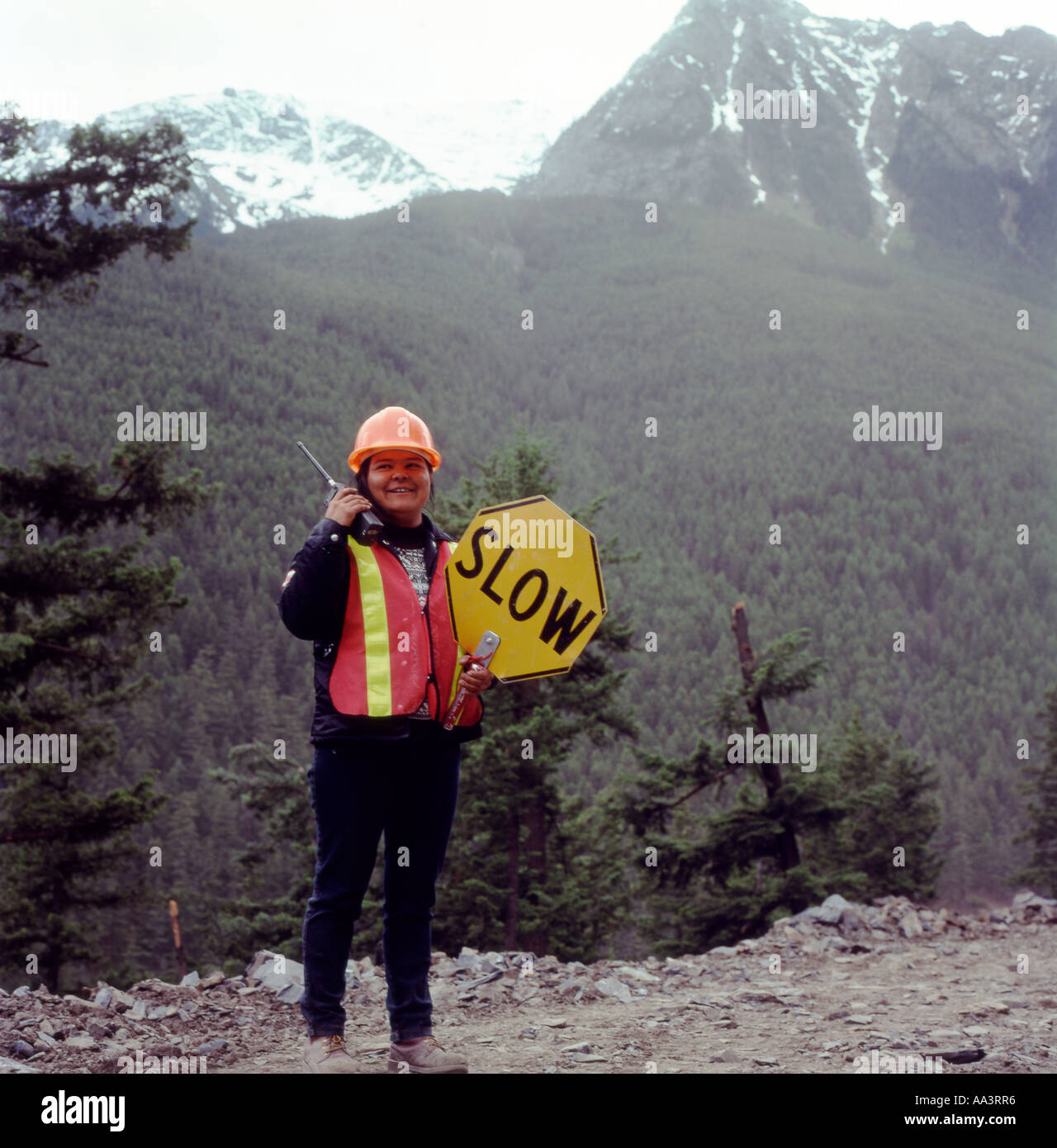 Eine Frau der First Nations im Straßenverkehr, die eine Langsamfahrt hält Verkehrszeichen und Handy auf einer Waldstraße Bau Standort in British Columbia, Kanada Stockfoto
