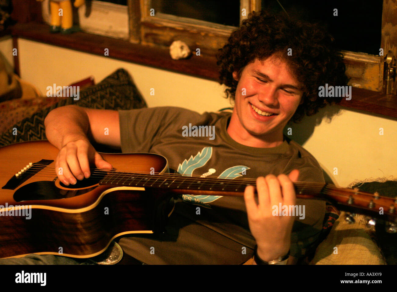 Ein teenboy lächelt, als er eine akustische Gitarre spielt Stockfoto