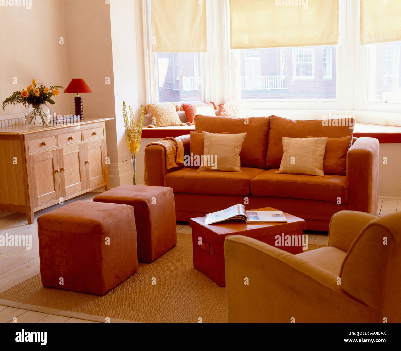 Modernes Wohnzimmer mit Terrakotta Sofa und gepolsterten Hocker und  cremefarbene Vorhänge an den Fenstern Stockfotografie - Alamy