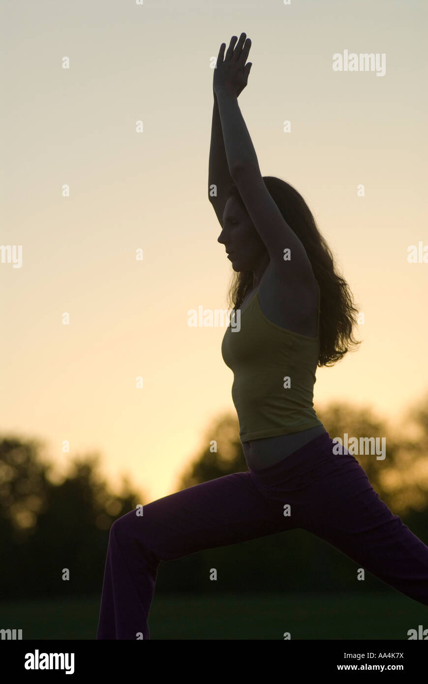 Silhouette einer jungen Frau, die beim Yoga bei Sonnenuntergang-Krieger 1 pose Stockfoto