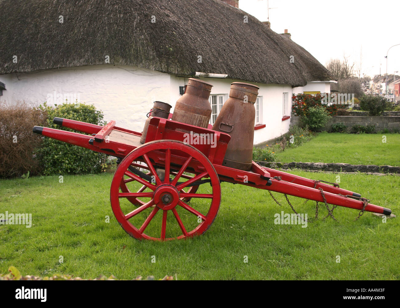 Rot-Handwagen mit Milchkanne und Reetdach-Ferienhaus Adare County Limerick Irland Stockfoto