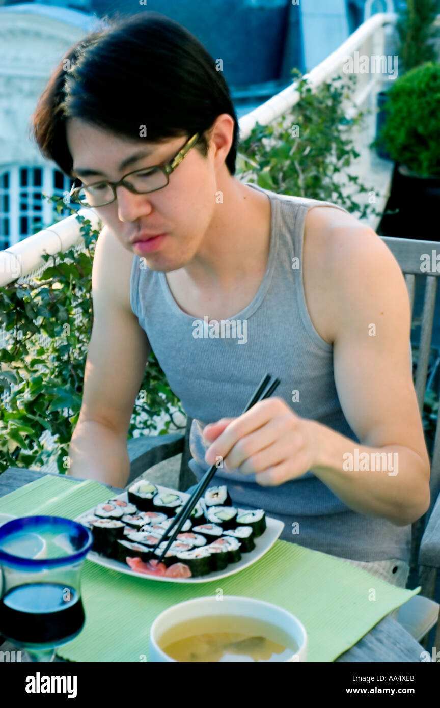 Porträt junger asiatischer Mann Essen, japanisches Essen Maki außen allein Sommer Stäbchen Stockfoto