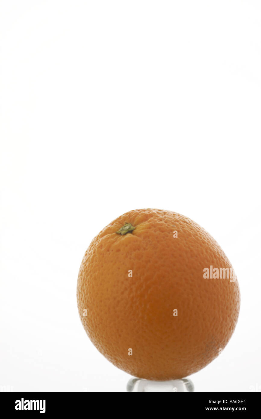 eine Orange auf weißem Hintergrund sitzt auf einer Basis Glasflasche Stockfoto