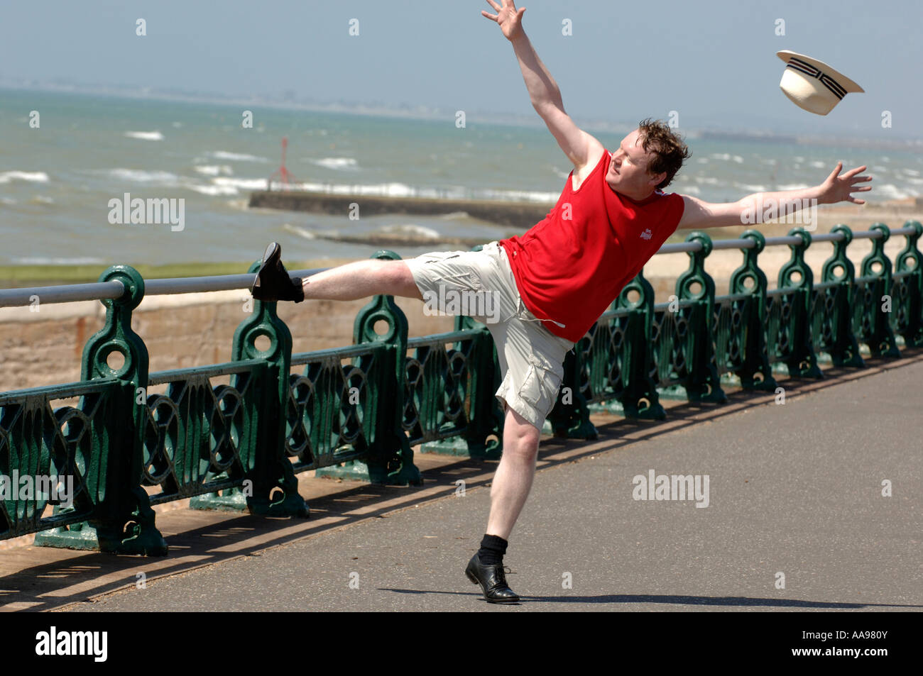 Ein übergewichtiger Mann mittleren Alters dabei ungeschickt hoch treten Tanzprogramm auf Brighton Seafront, wie seinen Hut in den Wind bläst aus Stockfoto