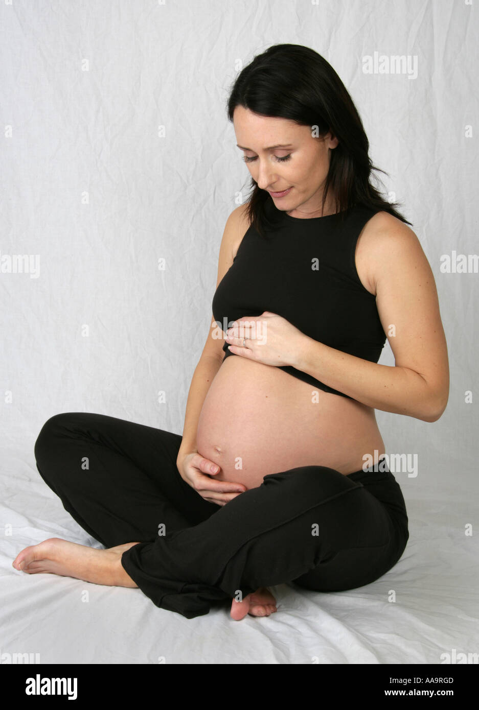 Schwangere Frau sitzen gekreuzt vierbeinigen trug eine schwarze Weste und Hose Stockfoto