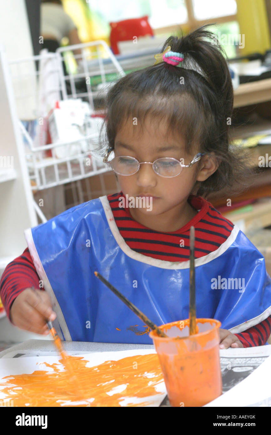 Grundschule Mädchen malen tragen blaue Malerei Kittel Stockfoto
