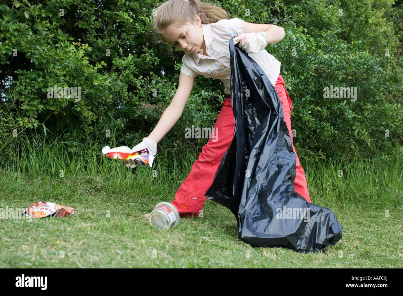 Zehn Jahre alte Blondine mit schwarzen Müllbeutel Abholung leere Flaschen und Müll im Park Cotswolds UK verworfen Stockfoto