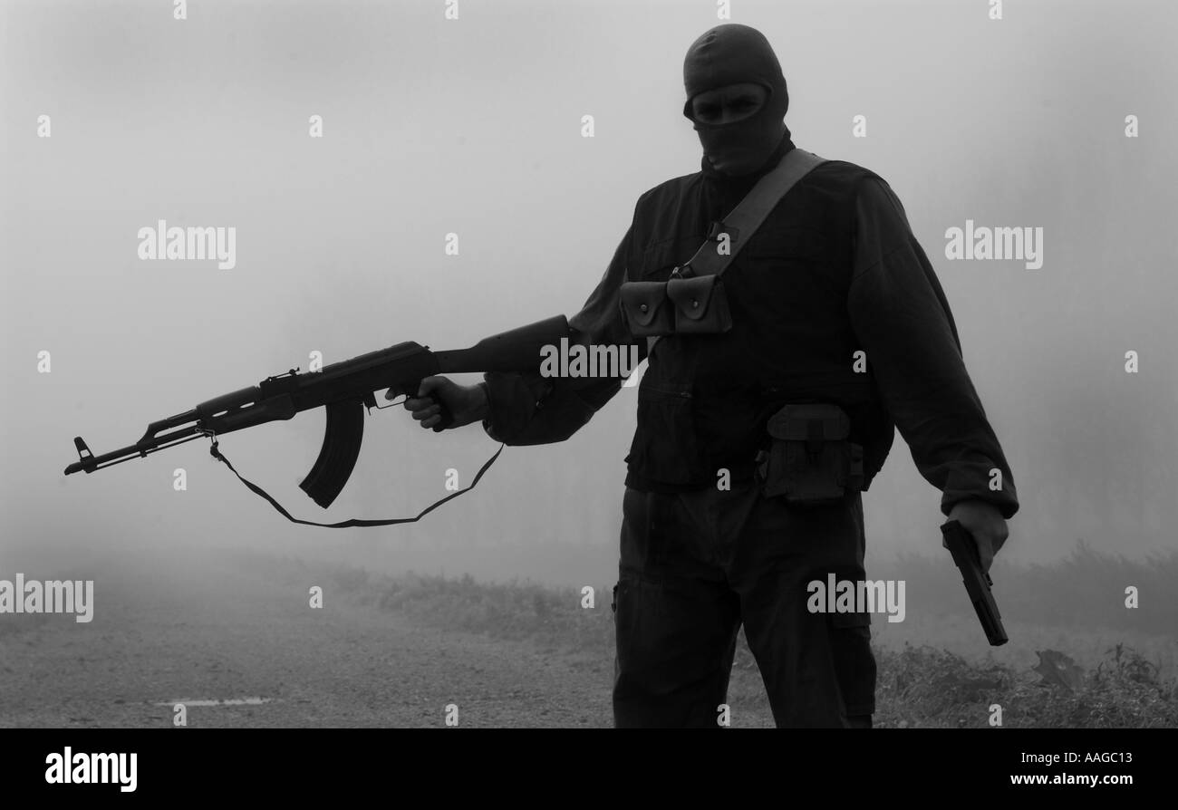Ein Terrorist, der in einer Sturmhaube gekleidet ist und ein Kalaschnikow-Gewehr AK47 hält und einen Gürtel aus Kugeln neben einem Land rover trägt, der VOM MODELL AUS AUFGESTELLT WIRD Stockfoto