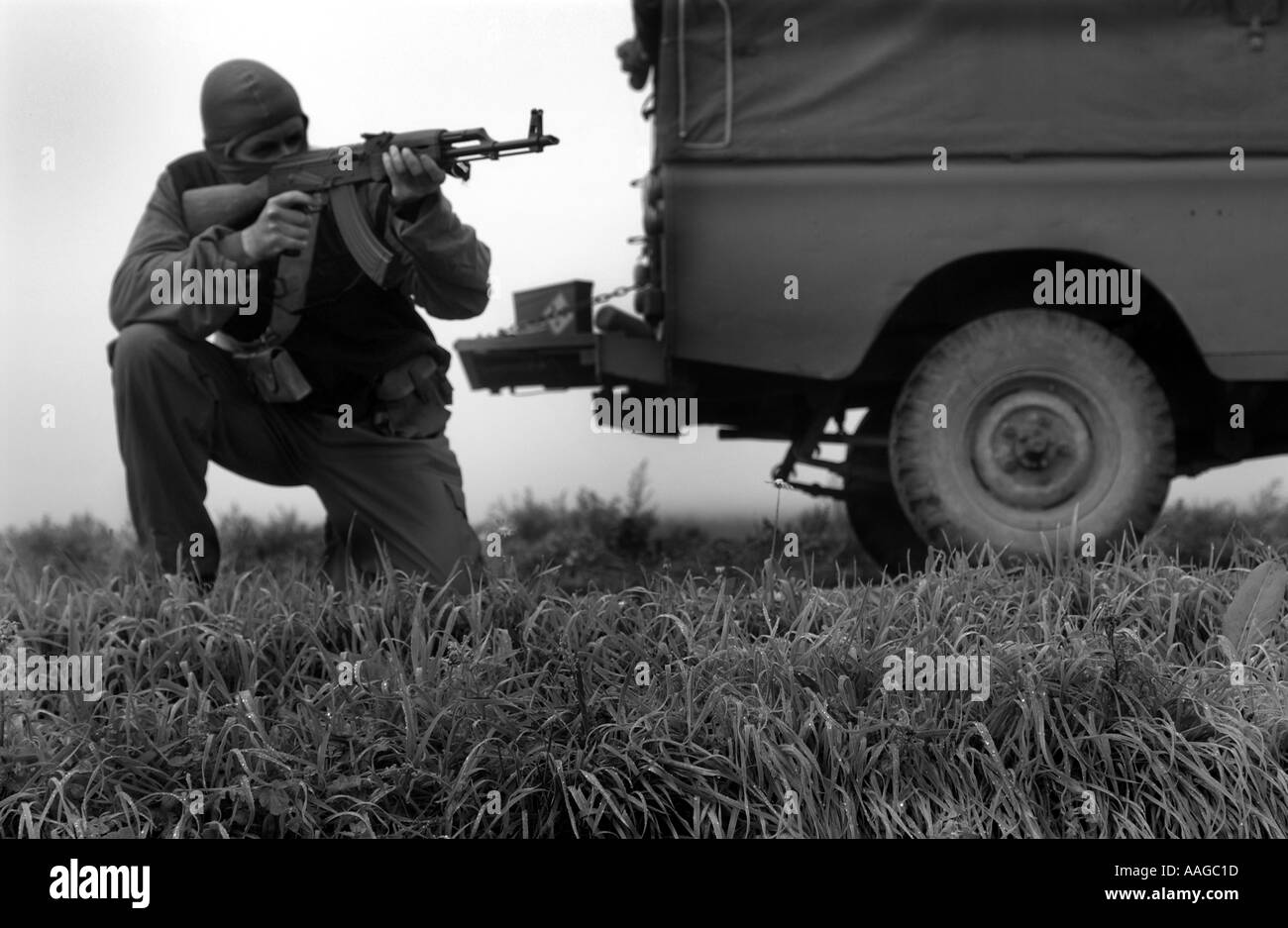 Ein Terrorist, der in einer Sturmhaube gekleidet ist und ein Kalaschnikow-Gewehr AK47 hält und einen Gürtel aus Kugeln neben einem Land rover trägt, der VOM MODELL AUS AUFGESTELLT WIRD Stockfoto