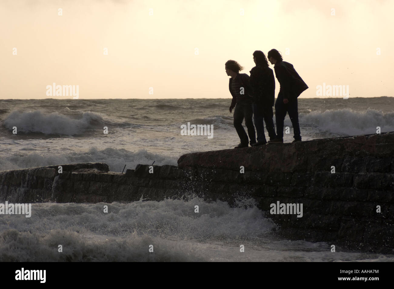 Silhouette von drei Personen junge Männer stehen auf steinernen Steg bei einem Sturm die Wellen ausweichen; Gesundheit und Sicherheit Risiko Stockfoto