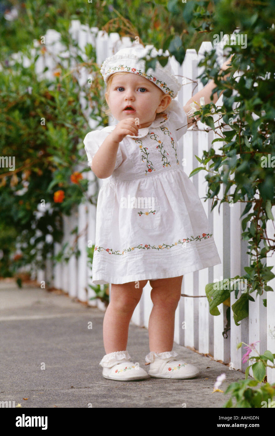 Babymädchen stehen von weißen Lattenzaun in liebenswert Kleid und Hut Stockfoto