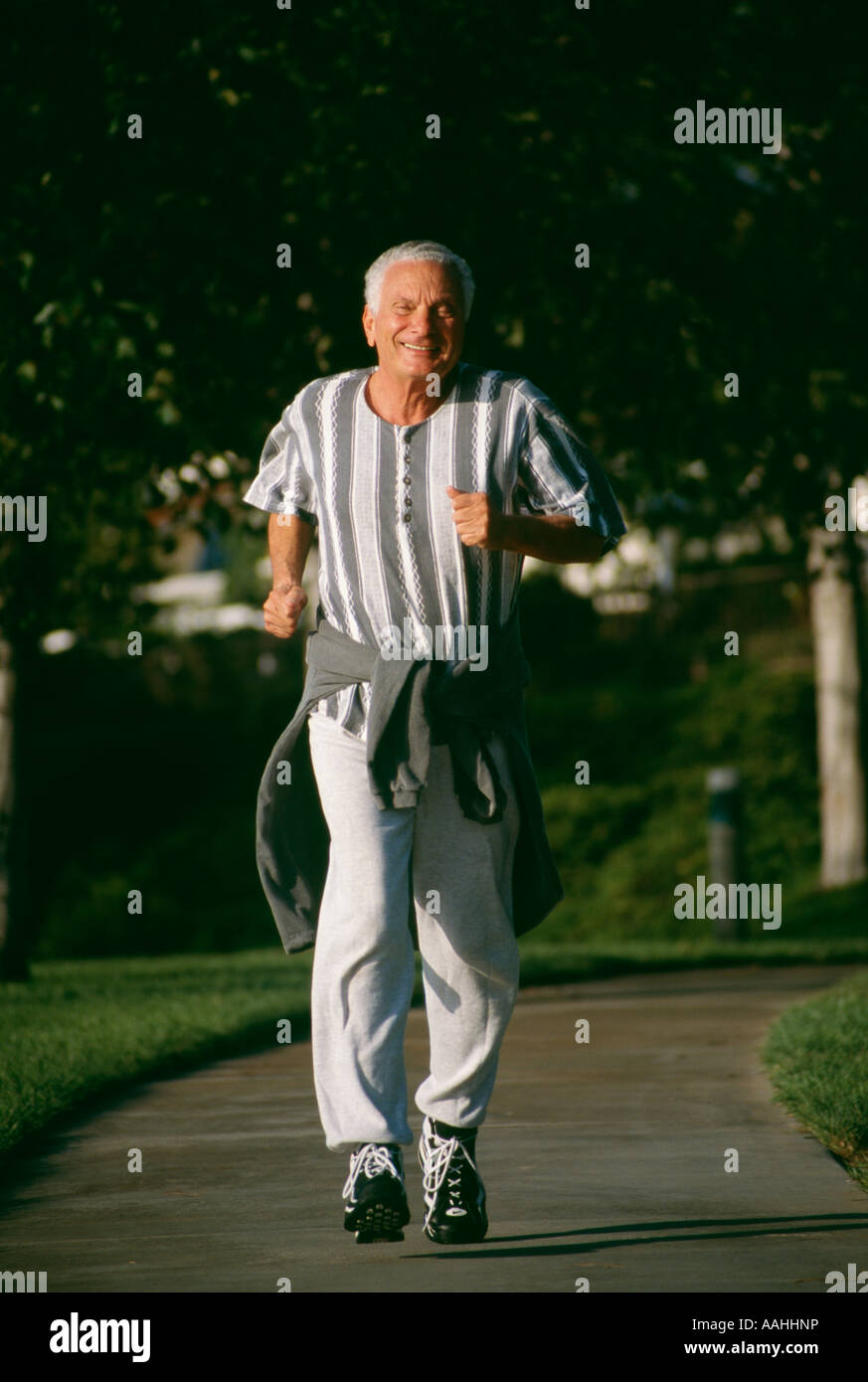 Eine lächelnde ältere Mann Bürger männlich 73 Jahre alte Ausübung Übung Energie energetische Sonne Brille Sonnenbrille im Park grüne textfreiraum POV Herr laufen Stockfoto