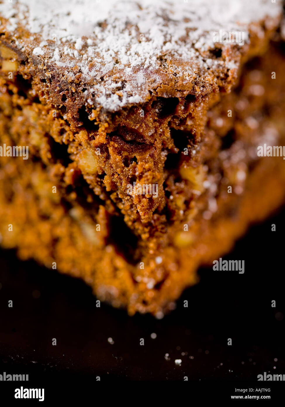 Nahaufnahme von bröckelig überbackenem Schokoladenbrownie, mit Puderzucker auf schwarzer Oberfläche bestäubt Stockfoto