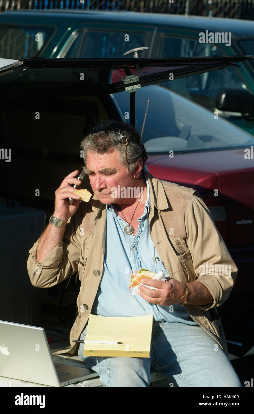 Fotograf-Gespräche über sein Handy beim Essen auf der Rückseite seines Trucks. Stockfoto