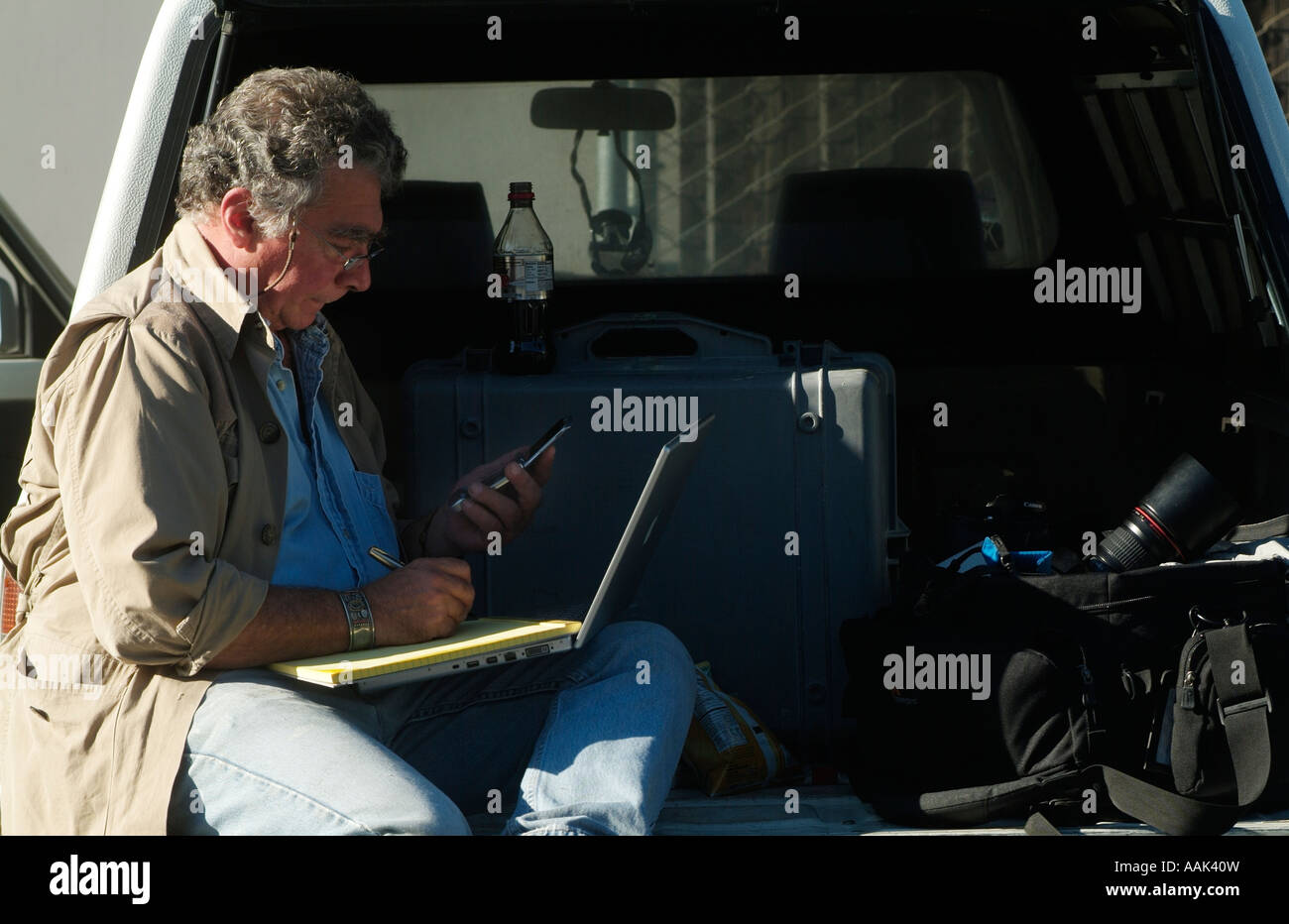 Fotograf mit seinem Handy, iMac-Computer und Notizblock beim Sitzen auf der Rückseite seines Trucks. Foto von Chuck Nacke Stockfoto