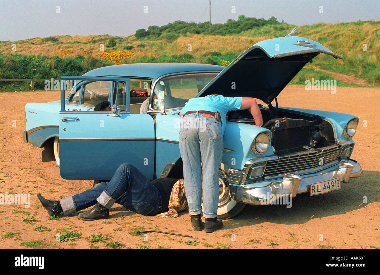 Junge Männer versuchen, ein alte blaue 1950er Jahre Auto am Strand Parkplatz während einer Rock'n'Roll zu reparieren "Roll Weekender-Festival. Stockfoto