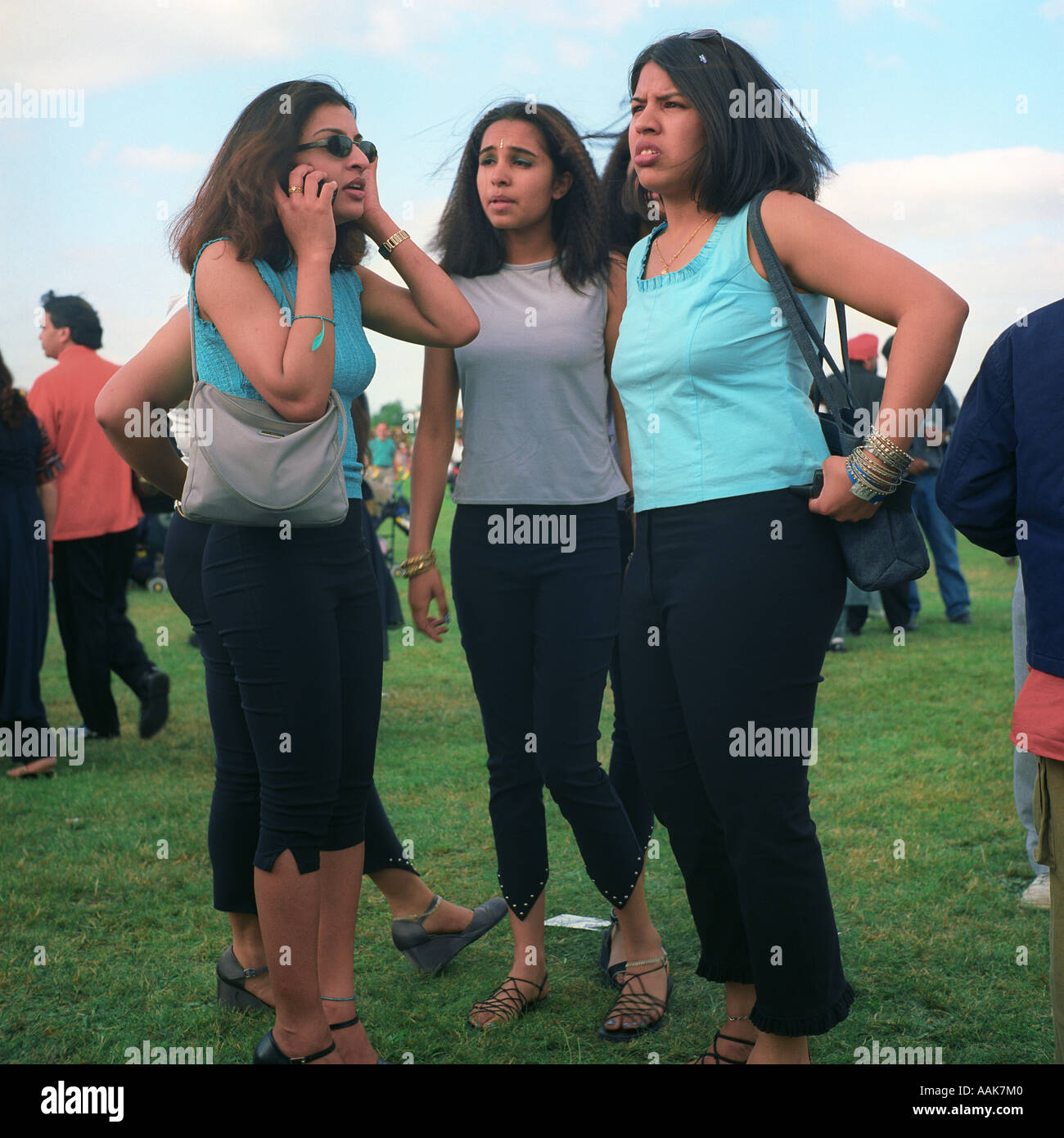 Vier asiatische Mädchen, ein Gespräch auf ein Mobiltelefon, an die East London Mela Wanstead Wohnungen, London, UK. Stockfoto