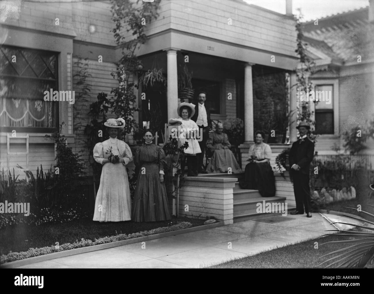 1890ER JAHRE 1900 S FAMILIE POSIERT FÜR FOTOGRAFIEREN AUßERHALB VERANDA DES HAUSES, BLICK IN DIE KAMERA Stockfoto