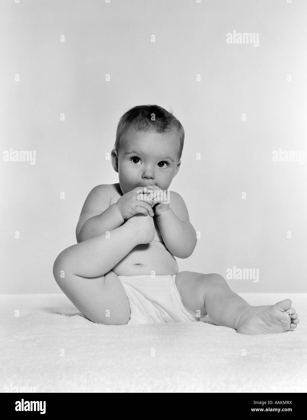 1950S 1960S BABY SITZEND AUF DECKE BRINGEN FUß IN DEN MUND Stockfoto