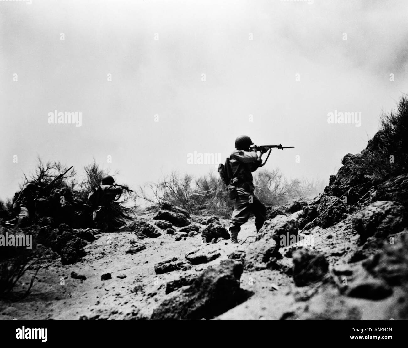 1940ER JAHRE BEKÄMPFUNG DER US ARMY INFANTERIE MÄNNER SCHIEßEN GEWEHRE IN AKTION MIT SCHWEREN RUCKSÄCKEN WÄHREND DES 2. WELTKRIEGES Stockfoto