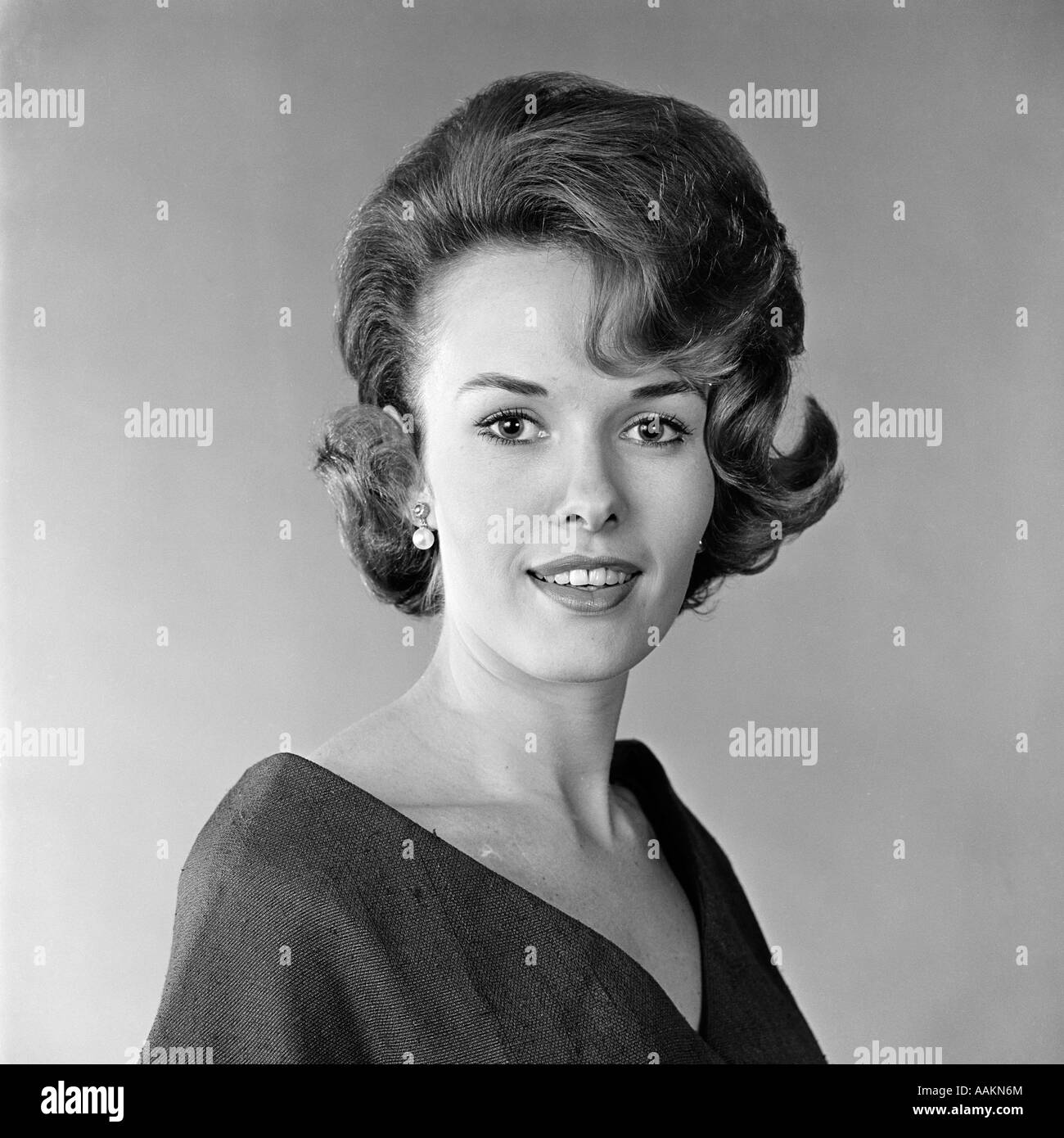 1960ER JAHRE PORTRÄT LÄCHELNDE FRAU BLICK IN DIE KAMERA MODISCHE FRISUR GEHÄNSELT Stockfoto