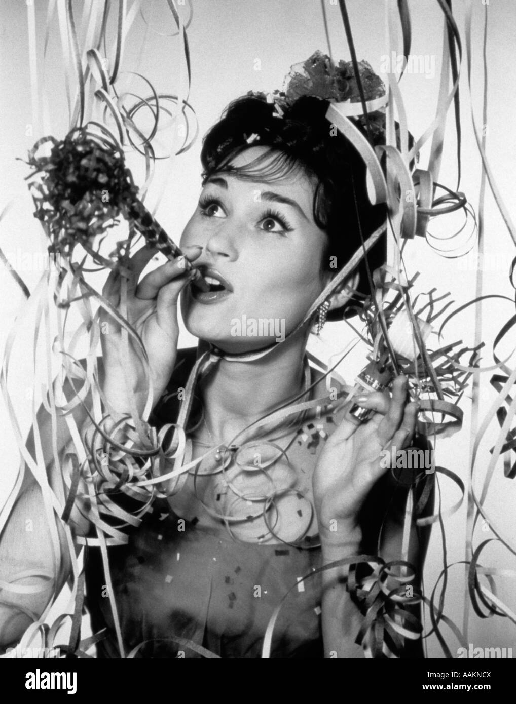 1950S 1960S FRAU BLÄST KRACHMACHER INMITTEN PARTY KONFETTI UND LUFTSCHLANGEN Stockfoto