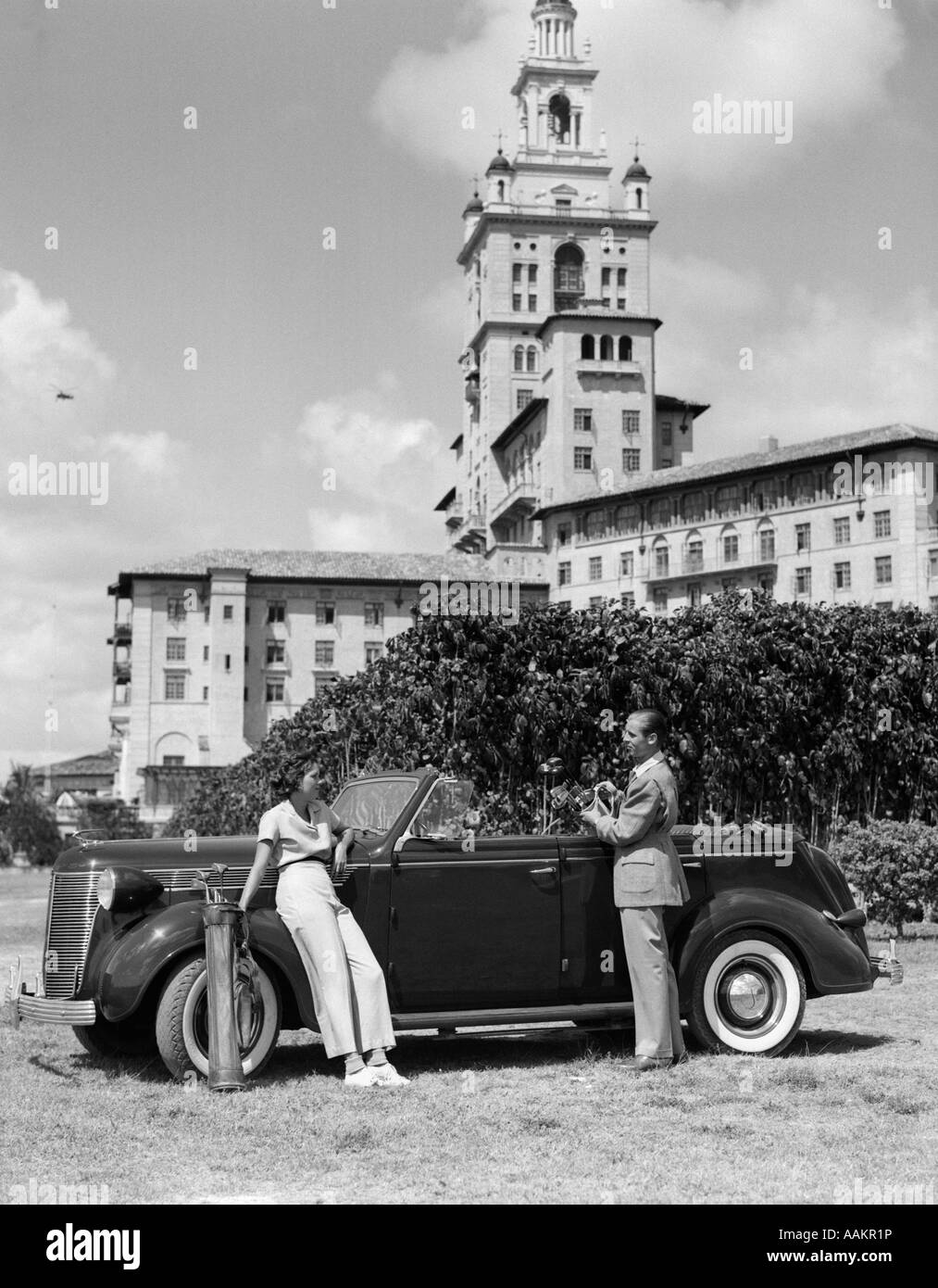 1930ER JAHREN PAAR MIT GOLF-CLUBS STAND EIN AUTO VOR DER BILTMORE HOTEL MIAMI FLORIDA Stockfoto