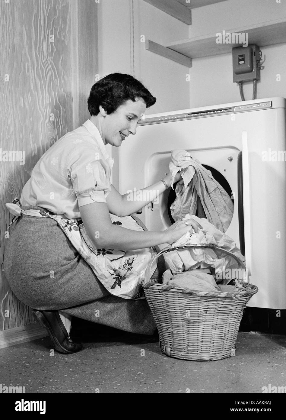 1950ER JAHREN FRAU KNIEND ENTFERNEN KLEIDUNG WÄSCHE AUS AUTOMATISCHE TROCKNER Stockfoto