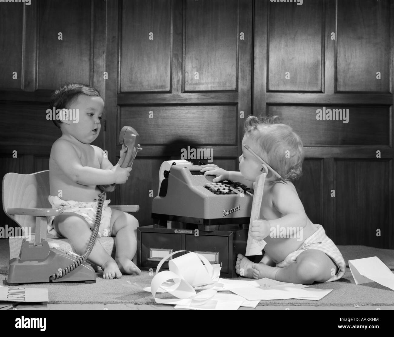1960ER JAHREN BLEISTIFT 2 BABYS IN WINDELN EIN ON STUHL MIT ANDEREN TELEFON ERDGESCHOSS MIT ADDING MACHINE HINTER OHR Stockfoto