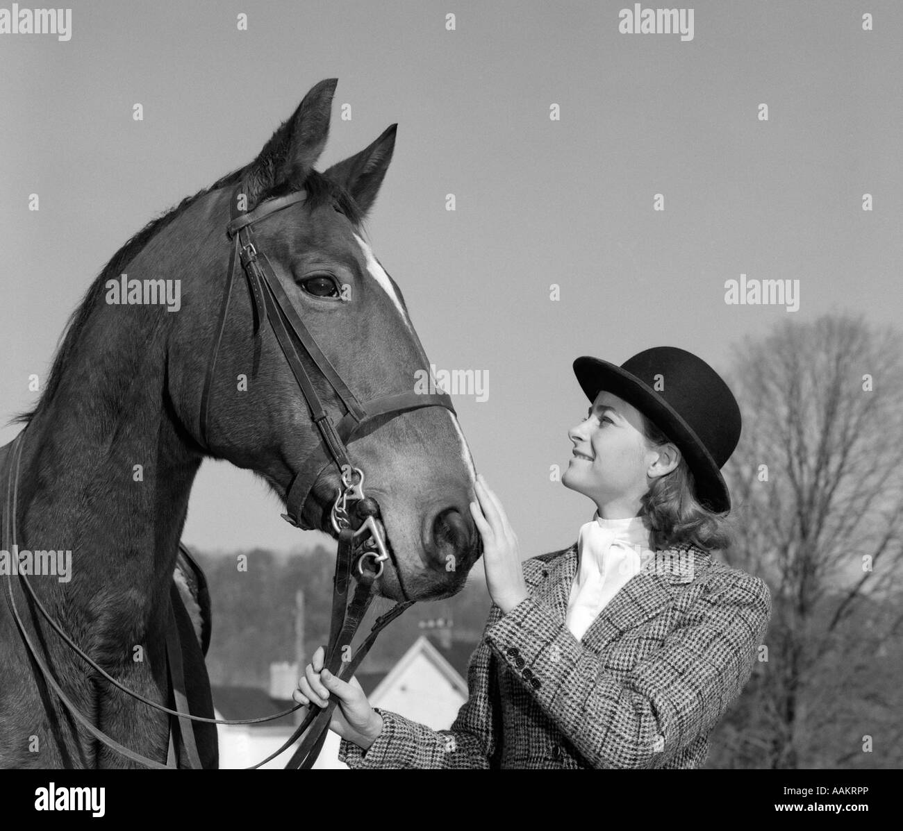 1960ER JAHREN FRAU IN ENGLISCHEN REITKLEID ZÜGEL DES PFERDES & STREICHELN SEINE NASE Stockfoto