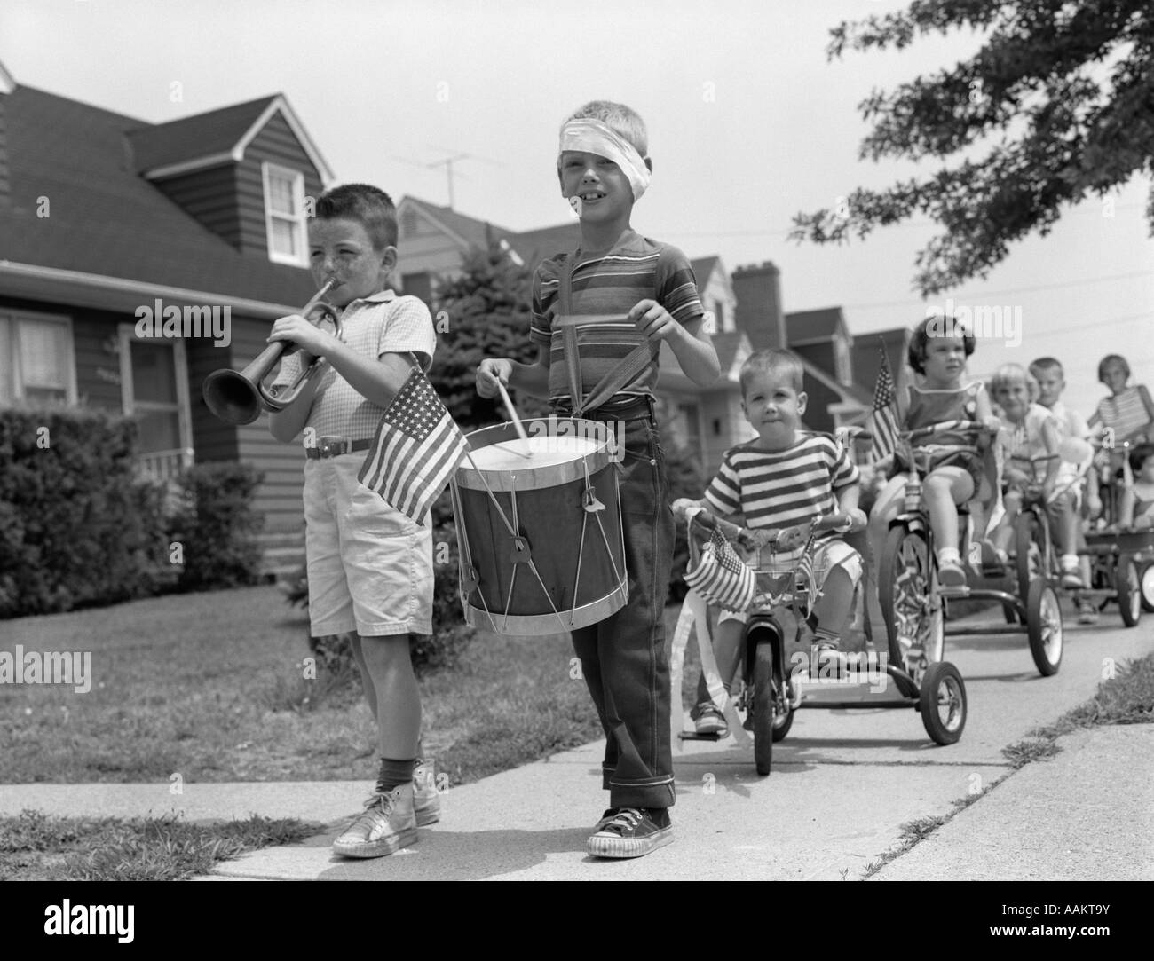 1960ER JAHREN KINDER IN VIERTEN JULI PARADE REITEN DREIRÄDER AUF BÜRGERSTEIG SPIELEN TROMMEL UND TROMPETE MUSIK Stockfoto