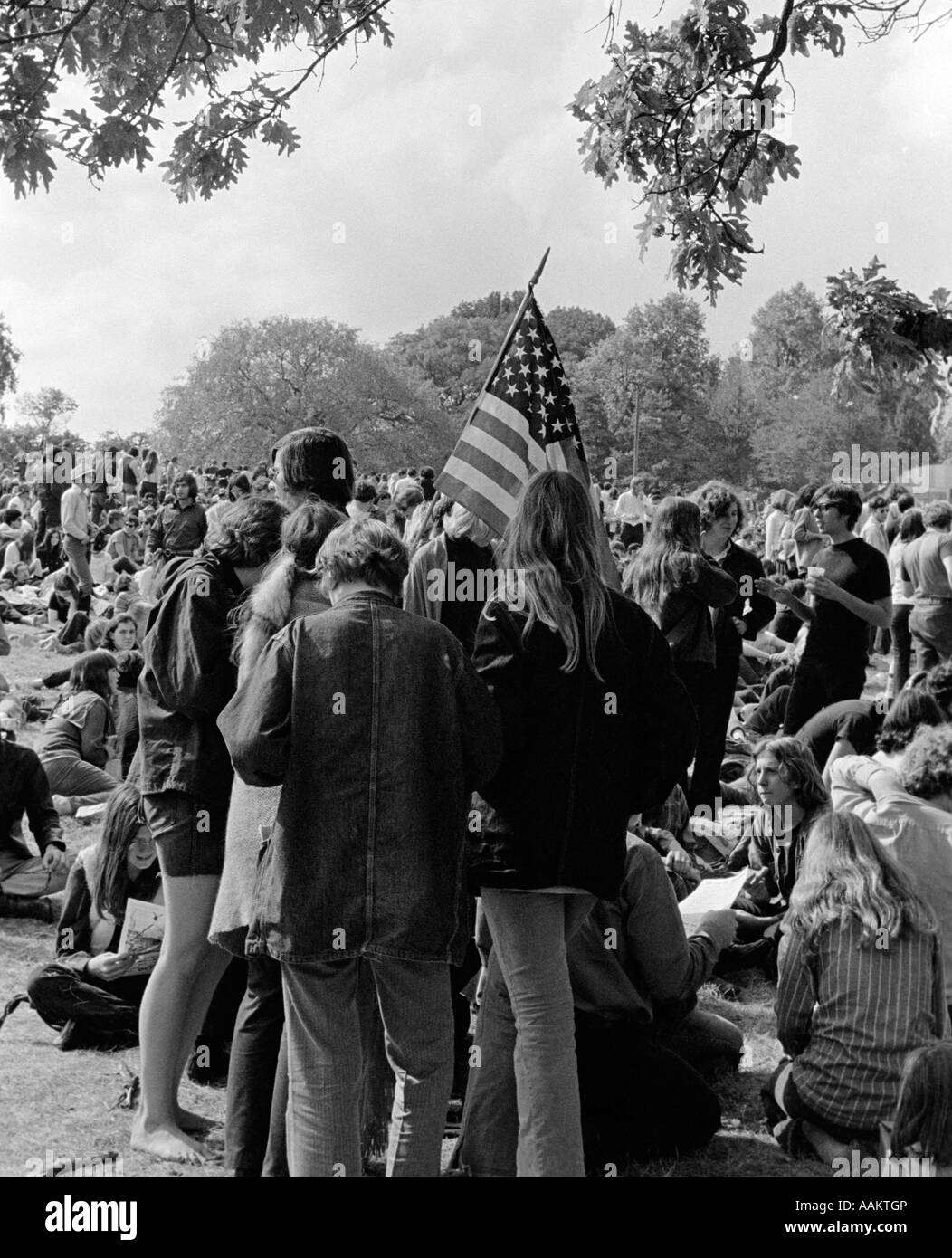 1970ER JAHREN RÜCKANSICHT DER SCHAR VON JUNGEN MÄNNER & FRAUEN TEENAGER STUDENTEN DIE TEILNAHME AN DER PROTESTDEMONSTRATION MIT AMERIKANISCHER FLAGGE Stockfoto