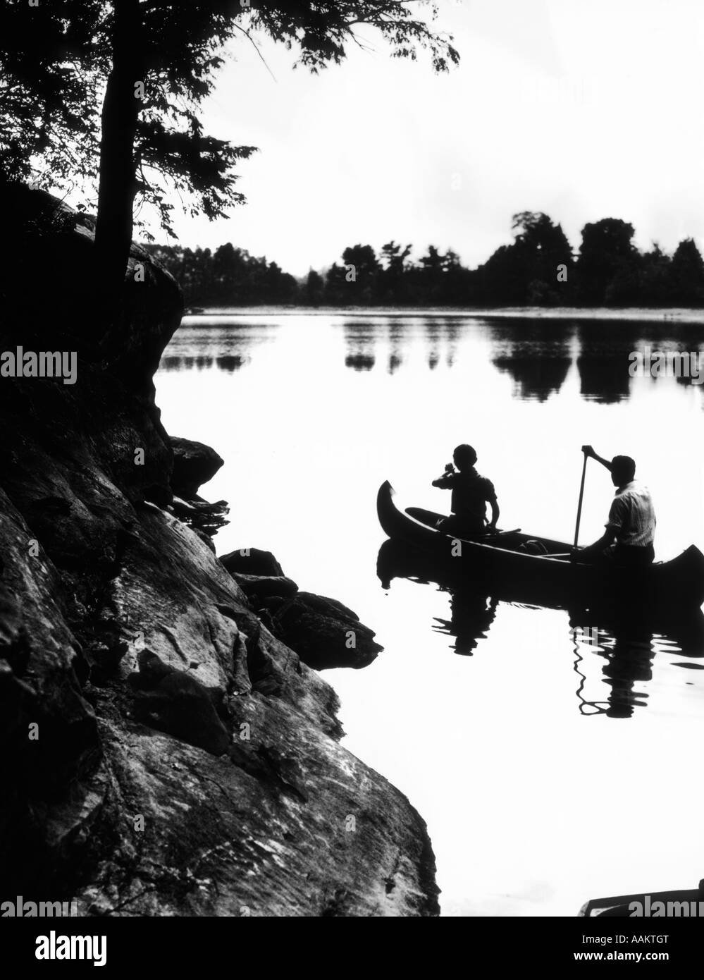 TONTRENNUNG PAAR KANU IM SEE, UMGEBEN VON FELSEN & BÄUME Stockfoto