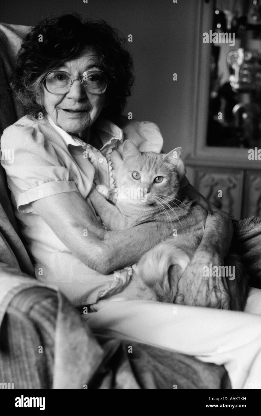 1980ER JAHRE SENIOR SENIORIN BRILLE HÄLT TABBY KATZE IN IHR ARME RUNDE PET GERIATRISCHE BEGLEITER ALTER THERAPIE TIER Stockfoto