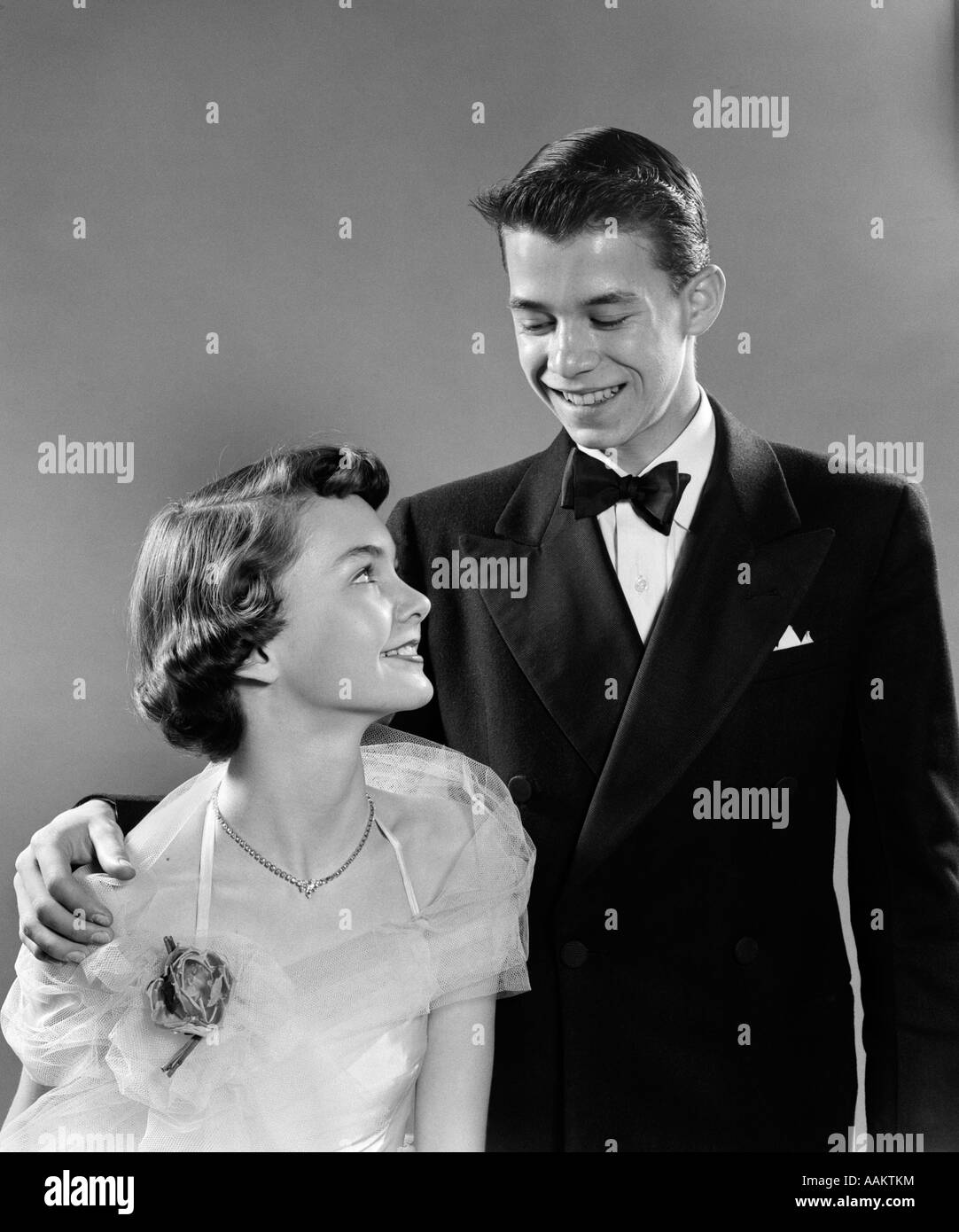 1950ER JAHRE JUNGES TEEN PAAR JUNGE MÄDCHEN IN FORMELLE KLEIDUNG FÜR HIGH-SCHOOL-ABSCHLUSSBALL Stockfoto